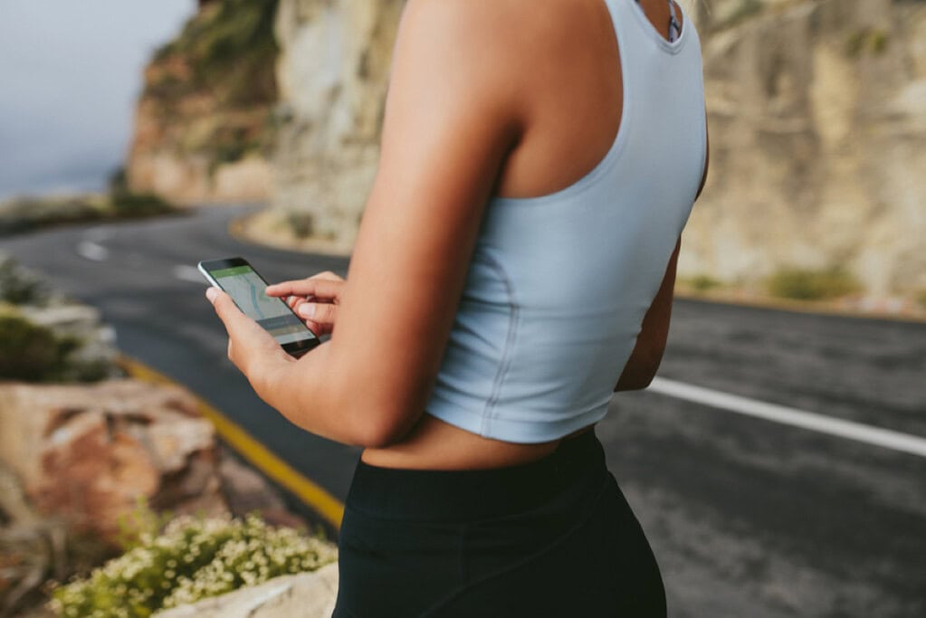 wellness tech - exercise tracking on smart phone - woman exercising outdoors