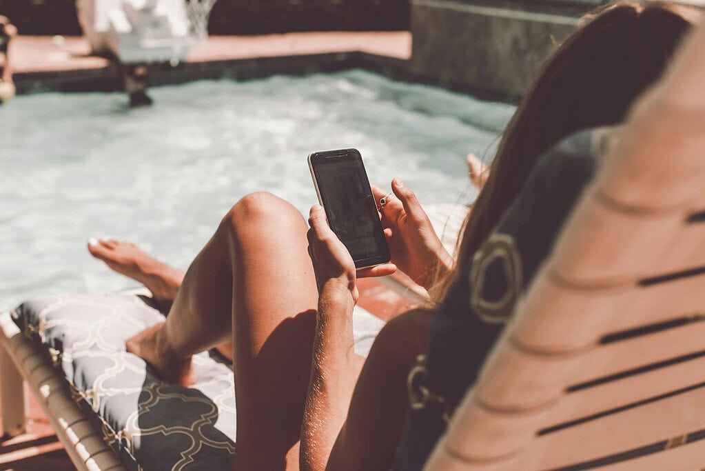 a woman enjoying life poolside with mobile in hand - self care apps