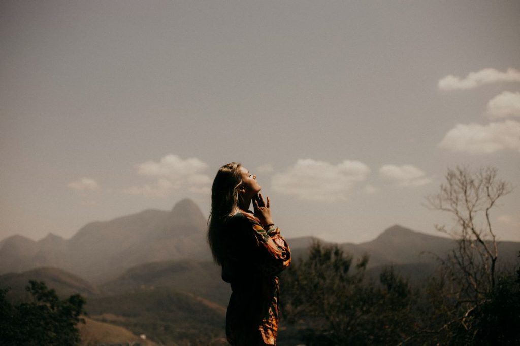 A woman standing on a hill with mountains in the background - what is anxiety featured image